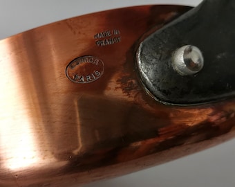 May include: Copper saucepan with a black handle and a silver rivet. The bottom of the pan is stamped with "Made in France" and "Cuivron Paris".