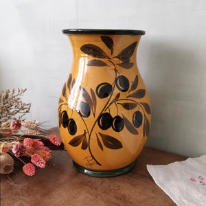 May include: A yellow ceramic vase with a black olive branch design. The vase has a green rim and base.