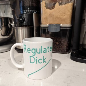 Puede incluir: Taza de café de cerámica blanca con un gráfico verde azulado que dice "Regulate Dick".