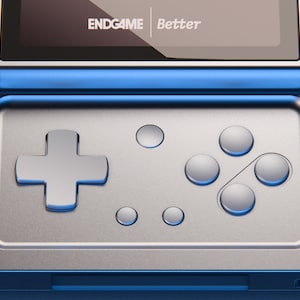 Könnte beinhalten: Eine silberne tragbare Spielkonsole mit metallischem Finish, einem Steuerkreuz, vier runden Aktionstasten und zwei kleineren Funktionstasten. Auf dem Bildschirm ist der Text ENDGAME Better in Weiß vor einem dunklen Hintergrund zu sehen.