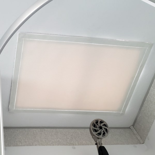 May include: A rectangular, frosted glass skylight is set into a white ceiling. The skylight is surrounded by a thin, white frame with a dotted pattern. A silver shower head is visible in the lower right corner.