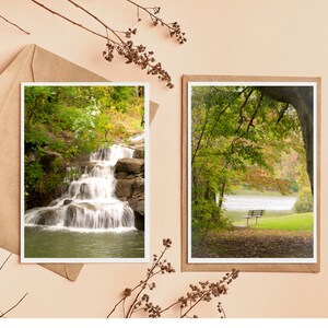 May include: Two landscape art prints featuring nature scenes. One print shows a waterfall cascading over rocks, surrounded by green foliage. The other print depicts a park scene with a bench near a lake, framed by trees with autumn colors.