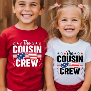 May include: Two children wearing matching red and white shirts with the text "The Cousin Crew" and an American flag design. The shirts are a patriotic theme for a family gathering.