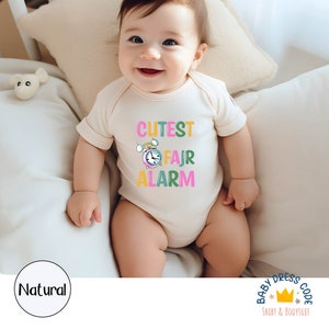 May include: A white baby onesie with a colorful graphic of an alarm clock and the text "Cutest Fajr Alarm".