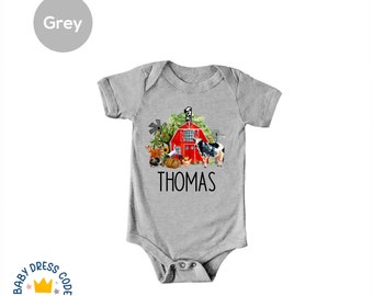 Puede incluir: Un body de manga corta gris con un gráfico de granero rojo y animales de granja. El texto "THOMAS" está impreso debajo del gráfico.