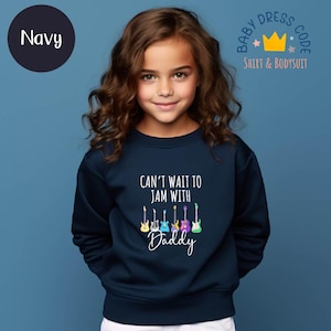 May include: Navy blue sweatshirt with the text "CAN'T WAIT TO JAM WITH Daddy" and colorful guitar graphics. The sweatshirt is part of the "Baby Dress Code" collection and is designed for children.