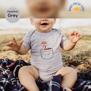 May include: A heather grey baby bodysuit with a cartoon snake in the pocket. The bodysuit has the text "Baby Dress Code" and "Shirt & Bodysuit" on the tag.