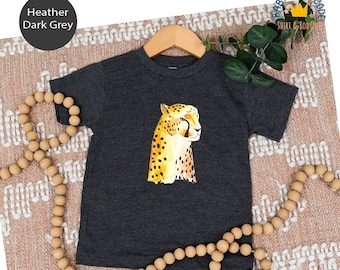 May include: A dark heather grey t-shirt featuring a cheetah print design. The shirt is displayed on a brown and white patterned surface.