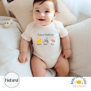 May include: A white baby bodysuit with the text "Future Triathlete" and illustrations of a rubber duck, a bicycle, and running shoes. The text "Swim, Bike, Run" is below the illustrations.