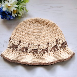 May include: A crocheted sun hat with a brown trim and a pattern of small animals around the brim. The hat is cream colored and made of a soft, textured yarn.