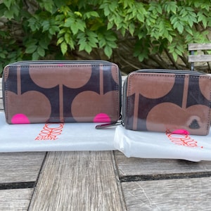 May include: Two brown and black patterned wallets with pink accents. The wallets have a zip-around closure and are placed on a white surface. The larger wallet is rectangular, and the smaller one is square. The wallets have a floral design.