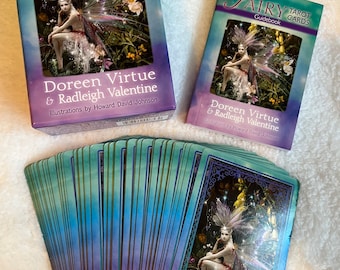 May include: A 78-card Fairy Tarot deck and guidebook with a purple, green, and gold color scheme. The box features an illustration of a fairy with wings and a flowing dress. The guidebook has a similar design with a different illustration of a fairy.