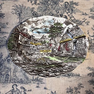Peut inclure: Un plat ovale en céramique présentant une scène détaillée et colorée de style transfert représentant un village rural anglais avec des chaumières, un château en pierre au loin et des personnages marchant sur un chemin, sur un tissu toile de Jouy.