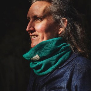 Puede incluir: Una mujer lleva un cuello de lana de color azul verdoso con una etiqueta blanca que dice "SIREN". Lleva una camisa vaquera azul oscuro.