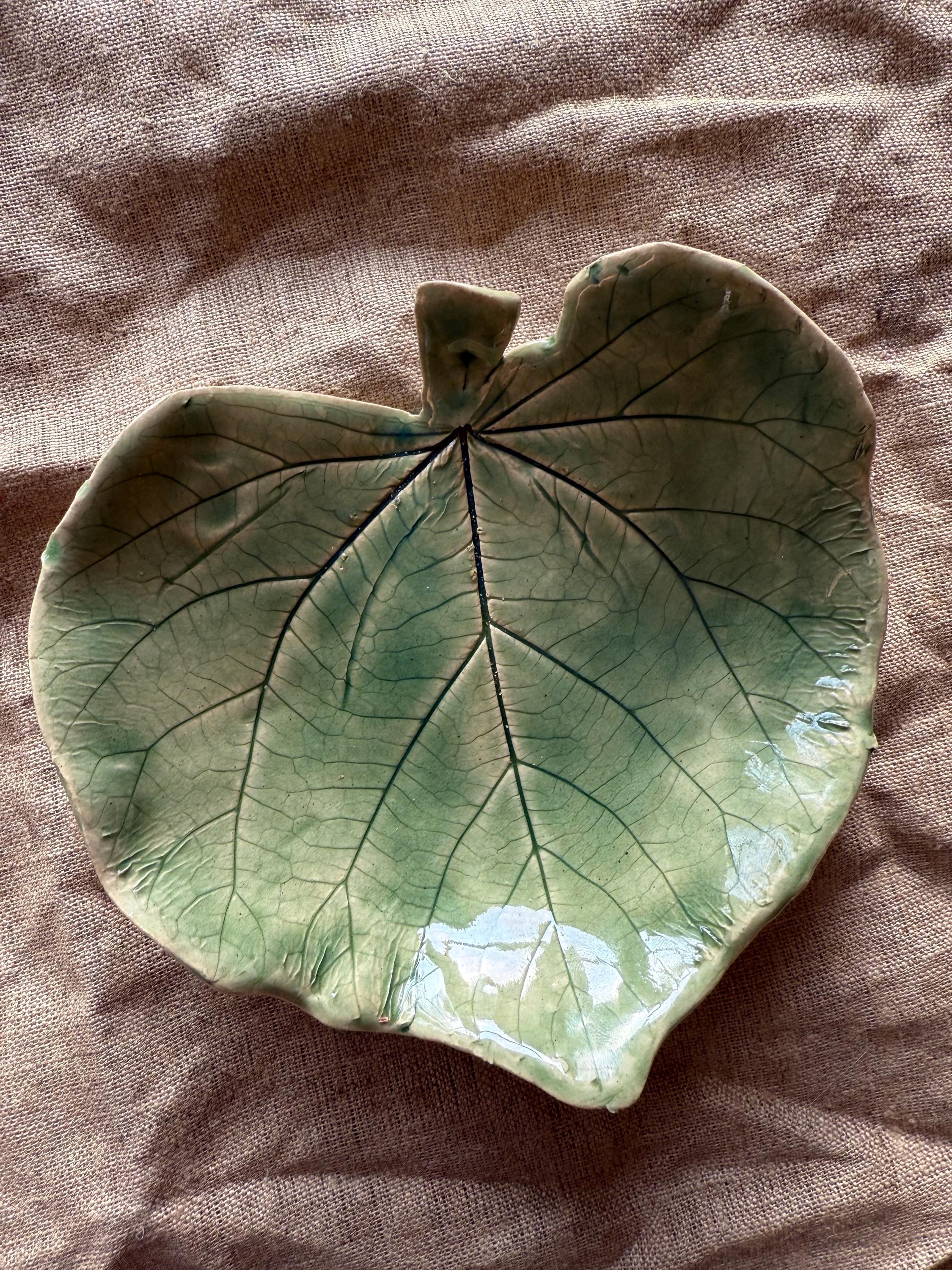 May include: A ceramic leaf-shaped dish with a green glaze and detailed veining. The dish is perfect for serving snacks or holding small items.