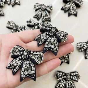 May include: A collection of black fabric bows decorated with silver and black rhinestones. The bows are approximately 2 inches in diameter.