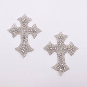May include: Two silver cross-shaped embellishments with clear rhinestones. The crosses are ornate and have a detailed design.