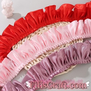 Pode incluir: Três camadas de guarnição com babados em vermelho, rosa e roxo. A guarnição é feita de tecido de cetim e tem um aspecto franzido.