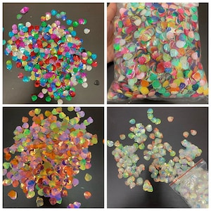 May include: Assortment of iridescent seashell-shaped sequins in various colors, including pink, blue, green, and rainbow. The sequins are packaged in clear plastic bags.