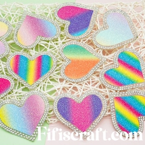 May include: Assortment of rainbow glitter heart-shaped patches with a rhinestone border. The hearts are in various shades of pink, purple, blue, and orange.