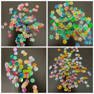 May include: Assortment of iridescent sequins in various shapes and sizes. The sequins are in shades of green, blue, pink, and yellow. Some sequins are round, while others are shaped like flowers.