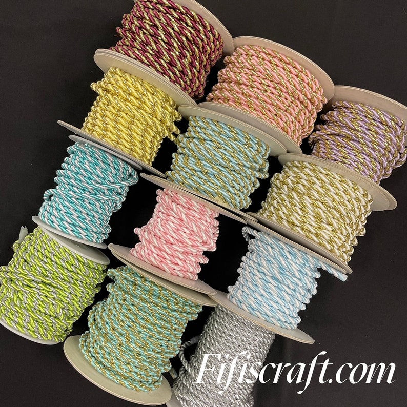 May include: A collection of twelve spools of twisted cord in various colours including burgundy, yellow, pink, lavender, turquoise, lime green, and silver, each featuring metallic gold or white threading. The text Fifiscraft.com is visible.