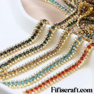 May include: A close-up of a variety of gold rhinestone chains with different colored rhinestones. The chains are arranged in a row, with the black rhinestone chain at the top and the red rhinestone chain at the bottom. The chains are all made of gold metal and have a shiny finish.