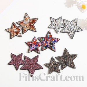 May include: Assortment of six pairs of star-shaped rhinestone embellishments. Each pair features a different color combination of rhinestones, including clear, brown, pink, black, and multi-colored.