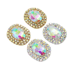 May include: Four iridescent oval-shaped rhinestones with a crystal-like appearance. Each rhinestone is surrounded by a border of small, sparkling crystals. Two have a gold-colored border, and two have a silver-colored border.