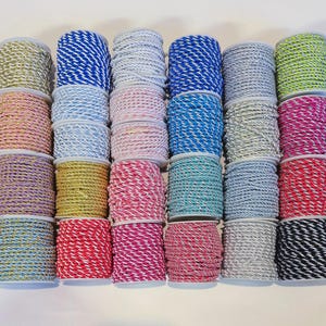 May include: A collection of twenty-four spools of twisted cord arranged in a grid. The cords feature various colour combinations including solid metallic gold, silver, neon green, and multi-coloured striped patterns in blue, pink, red, and black.
