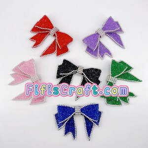 May include: A collection of glittery bows in various colors: red, purple, pink, black, green, and blue. Each bow features a rhinestone center and edges. The text "FifisCraft.com" is displayed across the image.