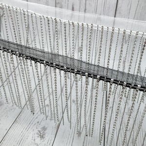 May include: Silver chain fringe trim with a black mesh backing. The fringe is made of small, round beads.