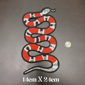 Puede incluir: Parche bordado de serpiente roja, negra y blanca. La serpiente está enroscada en posición vertical. El parche mide 14 cm x 24 cm.
