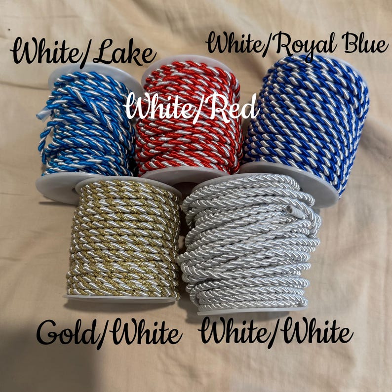 May include: Five spools of twisted cord in various colour combinations: White/Lake, White/Red, White/Royal Blue, Gold/White, and White/White. Each spool features a two-tone braided design with a metallic or solid finish, neatly wound on white plastic cores.