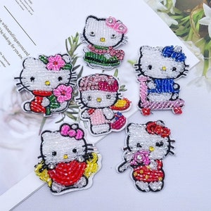 May include: Six colorful embroidered iron-on patches featuring Hello Kitty in different poses. The patches are made of white fabric with colorful beads and sequins.