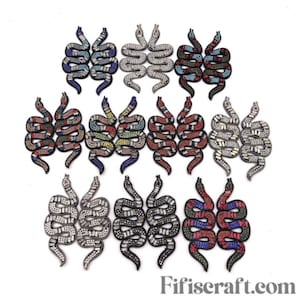 Puede incluir: Una colección de parches de serpiente con cuentas en varios colores, incluyendo azul, plateado, rojo y negro. Los parches están dispuestos sobre un fondo blanco. Los parches están adornados con pedrería y otros elementos decorativos.