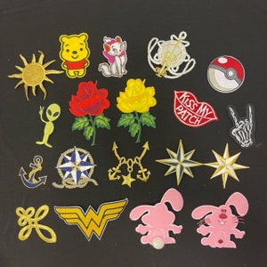 Könnte beinhalten: Eine Sammlung von 18 Bügelbildern mit verschiedenen Designs, darunter eine Sonne, ein Kompass, eine Rose, ein Schädel, eine Katze, ein Comic-Bär, ein Comic-Kaninchen, ein Stern, ein Anker, ein Peace-Zeichen, ein Herz und ein Wonder-Woman-Logo.