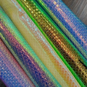 May include: Four rolls of iridescent mermaid scale fabric in shades of blue, green, and yellow. The fabric has a subtle shimmer and is perfect for crafting projects.