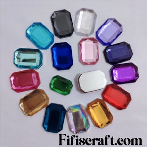 May include: Assortment of 15 colourful rectangular gem-shaped rhinestones in various colours including red, pink, blue, green, purple, gold, silver, and clear.