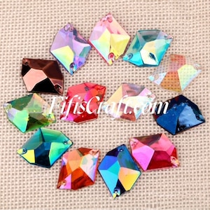 May include: Assortment of iridescent, faceted, diamond-shaped glass rhinestones in various colours, including red, blue, green, and brown. The rhinestones have two holes at the top for sewing or attaching.