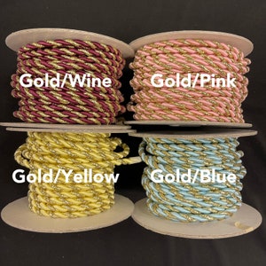 May include: Four spools of twisted cord trim, each featuring a metallic gold strand intertwined with a solid colour. The colours are labelled as Gold/Wine, Gold/Pink, Gold/Yellow, and Gold/Blue, with each spool displaying the corresponding text overlay.