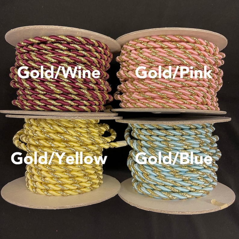 May include: Four spools of twisted cord trim, each featuring a metallic gold strand intertwined with a solid colour. The colours are labelled as Gold/Wine, Gold/Pink, Gold/Yellow, and Gold/Blue, with each spool displaying the corresponding text overlay.