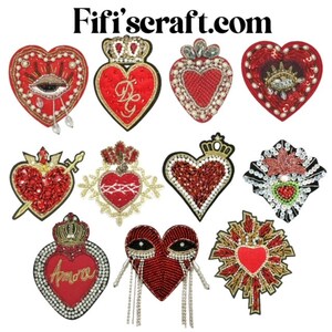 Könnte beinhalten: Sortiment von 10 roten herzförmigen Stickpatches mit verschiedenen Verzierungen, darunter Perlen, Pailletten und Strasssteine. Einige Patches zeigen Kronen, Pfeile und das Wort "Amore".