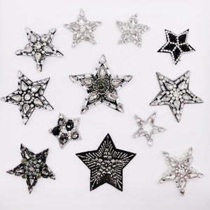 Può includere: Assortimento di 10 toppe a forma di stella da stirare con decorazioni in strass. Le toppe sono di diverse dimensioni e colori, tra cui nero, argento e trasparente.