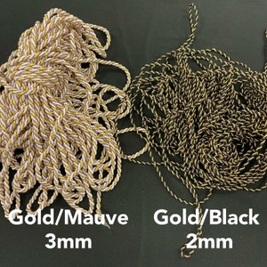 May include: Two bundles of twisted cord. The left bundle is gold and mauve with a 3mm thickness. The right bundle is gold and black with a 2mm thickness. Text below the cords reads Gold/Mauve 3mm and Gold/Black 2mm respectively.