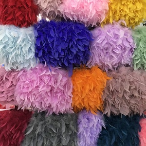 Puede incluir: Surtido de tejido de ribete de plumas de colores en varios tonos de rosa, azul, rojo, naranja, amarillo y gris. El tejido está dispuesto en un patrón de cuadrícula.