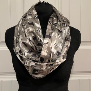 May include: A gray and black patterned infinity scarf with a satin finish. The pattern features stylized elephants.