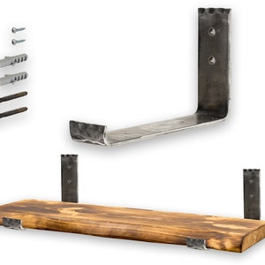 Op de afbeelding: Een rustiek houten plank met twee metalen beugels. De plank is gemaakt van natuurlijk hout met een ruwe, onafgewerkte uitstraling. De beugels zijn gemaakt van zwart metaal en hebben een gehammerde afwerking. De plank wordt ondersteund door twee metalen beugels die met schroeven aan de muur zijn bevestigd. De plank is perfect voor het tentoonstellen van boeken, planten of andere decoratieve items.