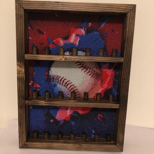 May include: A wooden frame with three shelves for displaying baseballs. The back of the frame features a colorful diamond painting of a baseball with red, white, and blue paint splatters.
