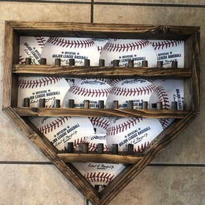 Könnte beinhalten: Ein hölzerner Baseball-Präsentationsständer in Form einer Homeplate mit neun Baseballs auf zwei Regalen. Die Baseballs sind weiß mit roten Nähten und haben den Text "Official Major League Baseball" aufgedruckt.